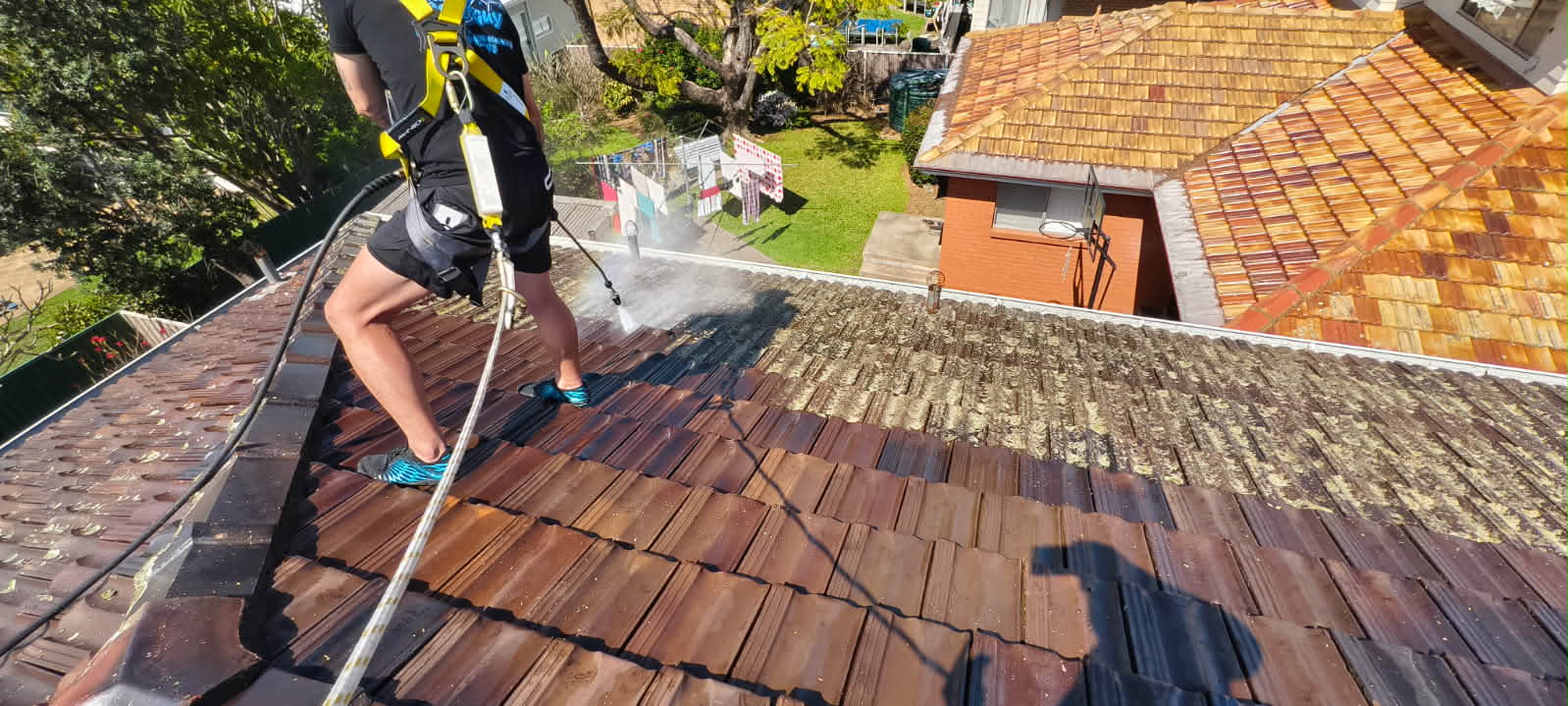 Damien soft-washing a terracotta tiled roof, the cleaned half showing a sharp line against the moss